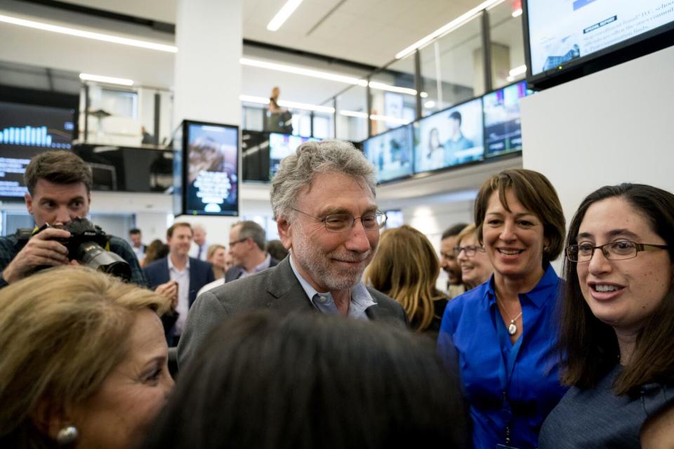 People stand in a two-story open newsroom looking happy.
