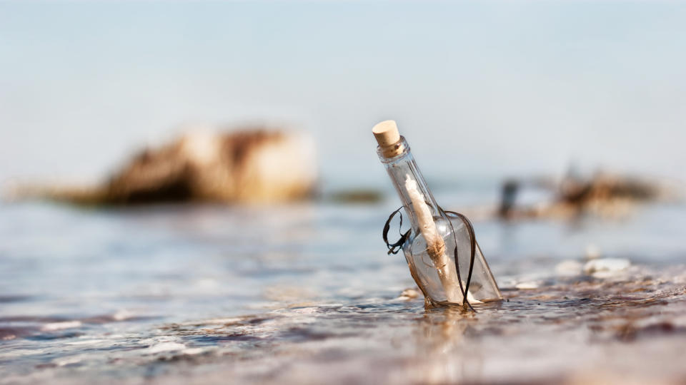 List auf Sylt, Schleswig Holstein, Germany - April 30, 2012: A message in a bottle floating in shallow water. Sunshine, blue sky and rocks in the background