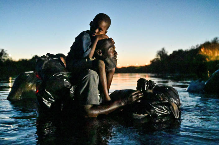 A man carries a child on his shoulders as Haitian migrants cross the Rio Grande river between Mexico and Del Rio, Texas, on Sept. 23, 2021. (Pedro Pardo / AFP via Getty Images)