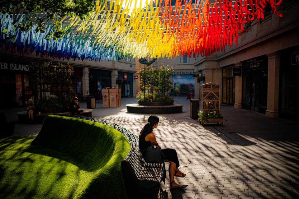 <p>A person sits beneath rainbow coloured street decorations as the strong morning sun casts shadows on the floor in Bath city centre. Picture date: Wednesday September 8, 2021.</p>
