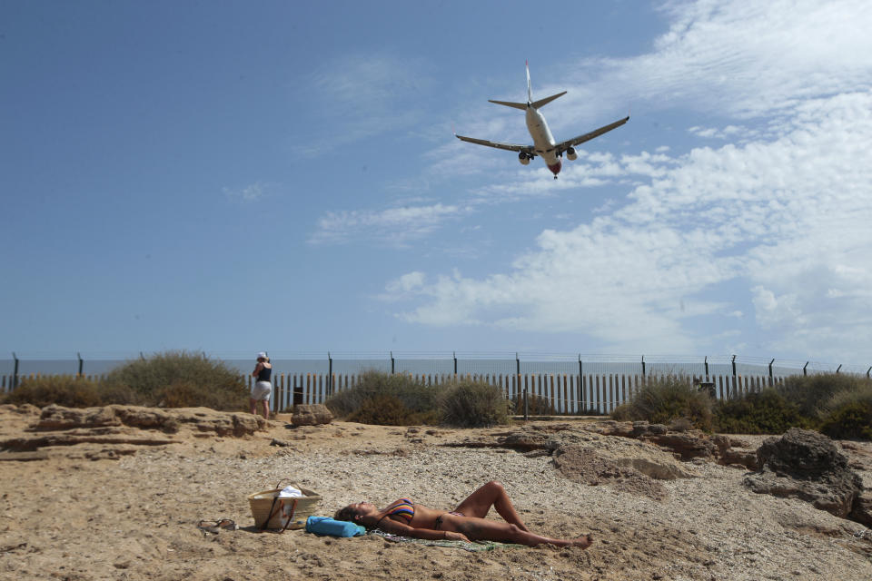 FILE - In this Wednesday, July 29, 2020 file photo, a woman sunbathes on the beach as an airplane lands at the Balearic Islands capital of Palma de Mallorca, Spain. Faced with a possible flood of visitors from Germany later this month, authorities in Spain’s Balearic Islands are warning hotel owners that tourists must adhere to coronavirus restrictions the same way residents do. The archipelago in the Mediterranean Sea is strengthening measures to combat the virus before the Easter period. But the restrictions haven’t stopped eager German tourists who have rushed to book flights and accommodation this week following their government’s removal of the islands from a list of high-risk contagion zones. (AP Photo/Joan Mateu, File)