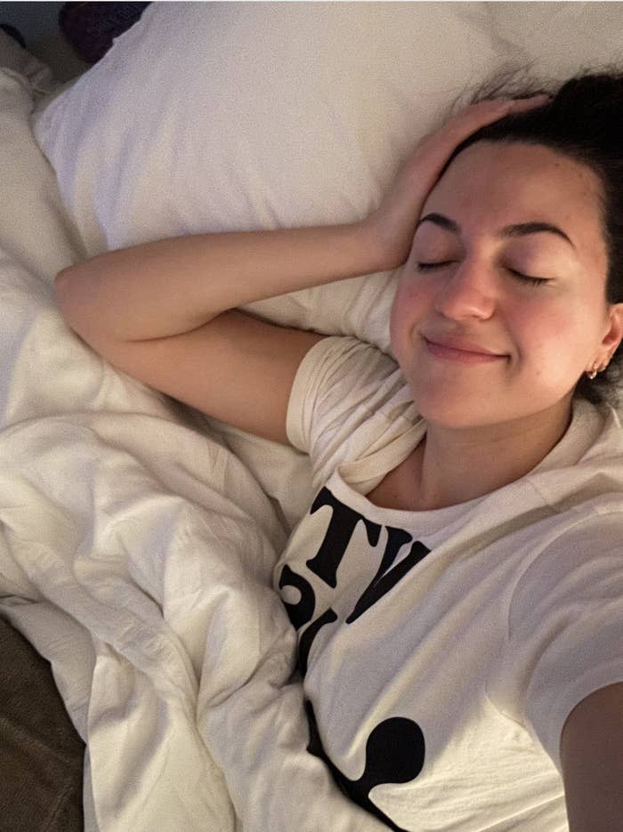 Person lying in bed with eyes closed, head resting on hand, wearing a T-shirt with lettering