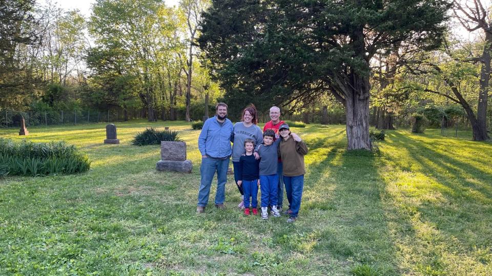 James and Makaela Smith and their sons Linus and Samuel stand in McElhaney Cemetery with Gene Davison and Linda Halford on April 30, 2023. Davison and Halford have taken care of the cemetery as volunteers since 1997, and are now stepping down due to their age. The Smiths are taking over as volunteer caretakers.