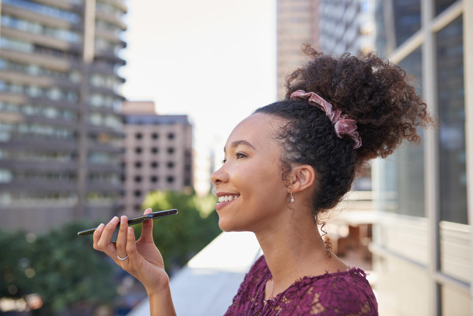 A young woman sends a voicenote on the balcony of an office building in the city