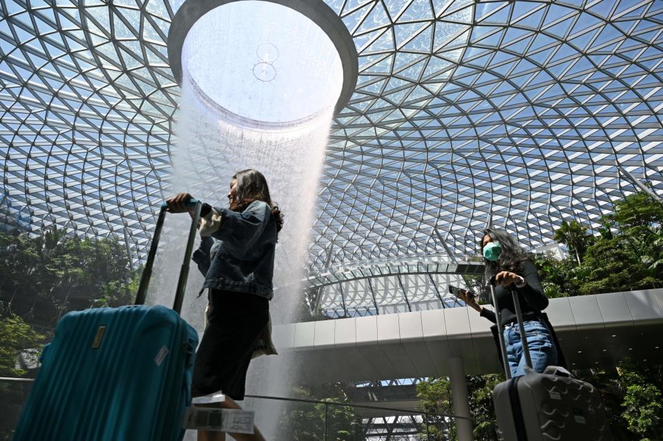 A traveller (R), wearing a protective facemask amid fears about the spread of the COVID-19 novel coronavirus, walks past the Rain Vortex display at Jewel Changi Airport in Singapore on February 27, 2020. (Photo by Roslan RAHMAN / AFP) (Photo by ROSLAN RAHMAN/AFP via Getty Images)