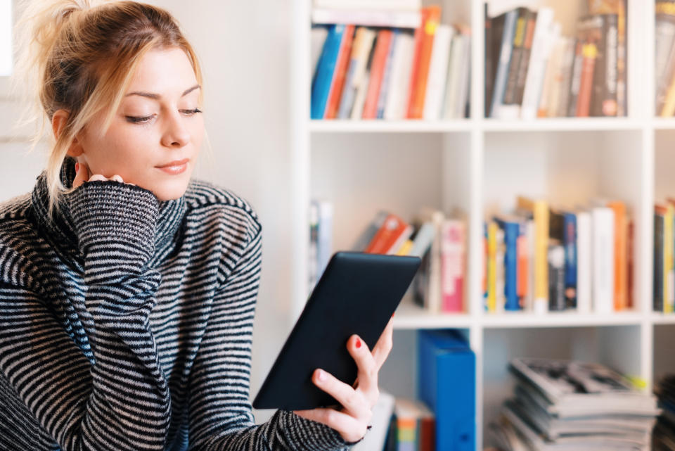 Young student using e-book and bookshelf on background