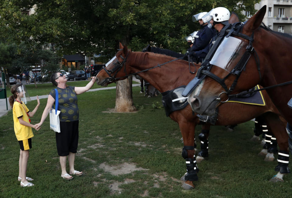 A woman touches a police horse during a demonstration in Belgrade, Serbia, Wednesday, July 8, 2020. Serbia's president Aleksandar Vucic backtracked Wednesday on his plans to reinstate a coronavirus lockdown in Belgrade after thousands protested the move and violently clashed with the police in the capital. (AP Photo/Darko Vojinovic)