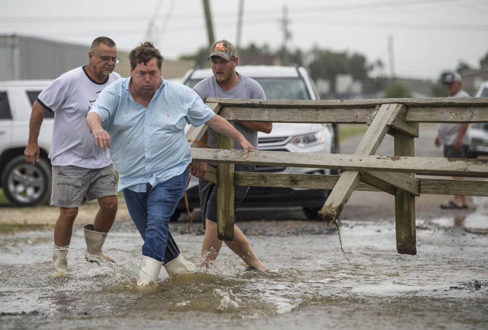 Louisiana Lt. Gov. Billy Nungesser, left center, helps move a wooden barricade to block a road where water was rising in Plaquemines Parish just south of New Orleans as Hurricane Barry makes landfall along the coast on Saturday, July 13, 2019. (Chris Granger/The Advocate via AP)