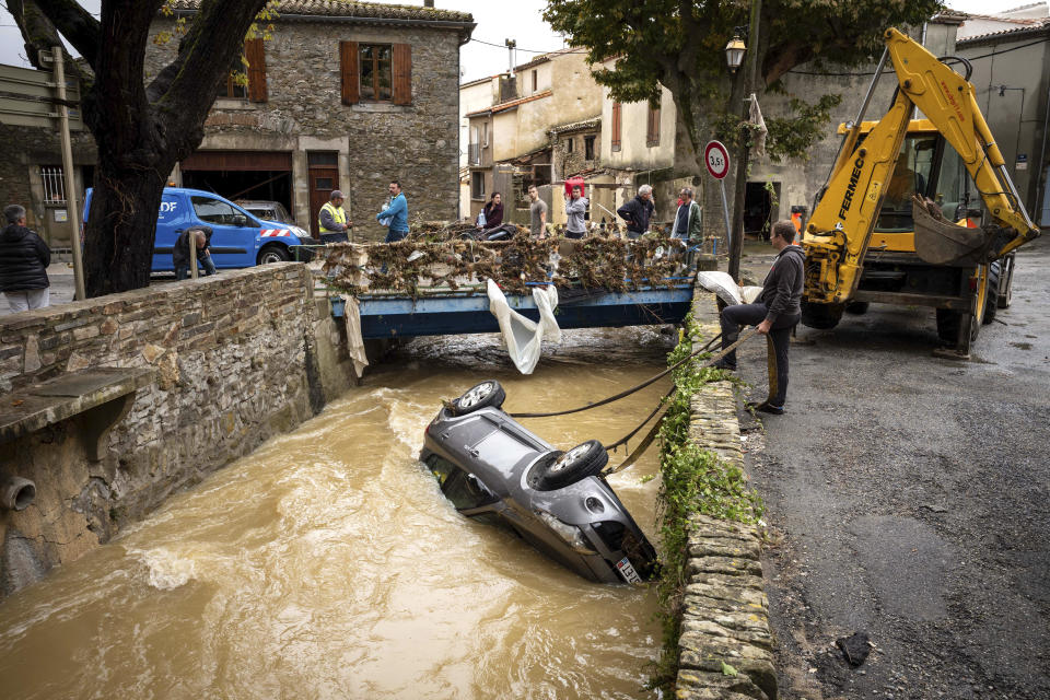 People try to pull a car out of a torrent after flash floods in the town of Villegailhenc, southern France, Monday, Oct.15, 2018. Flash floods tore through towns in southwest France, turning streams into raging torrents that authorities said killed several people and seriously injured at least five others. (AP Photo/Fred Lancelot)