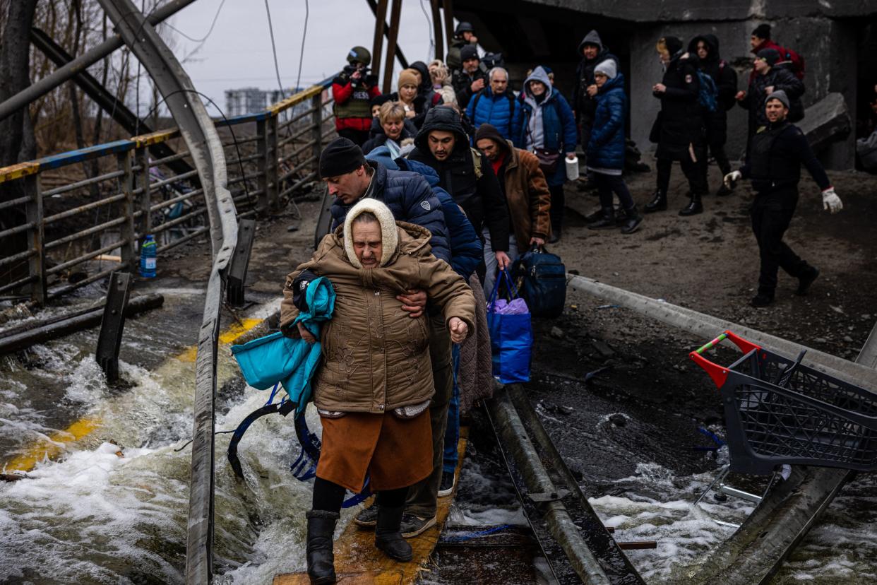 A man helps a woman evacuee cross a destroyed bridge as she and others flee the city of Irpin, northwest of Kyiv, on March 7, 2022. (Photo by Dimitar Dilkkoff/AFP via Getty Images)