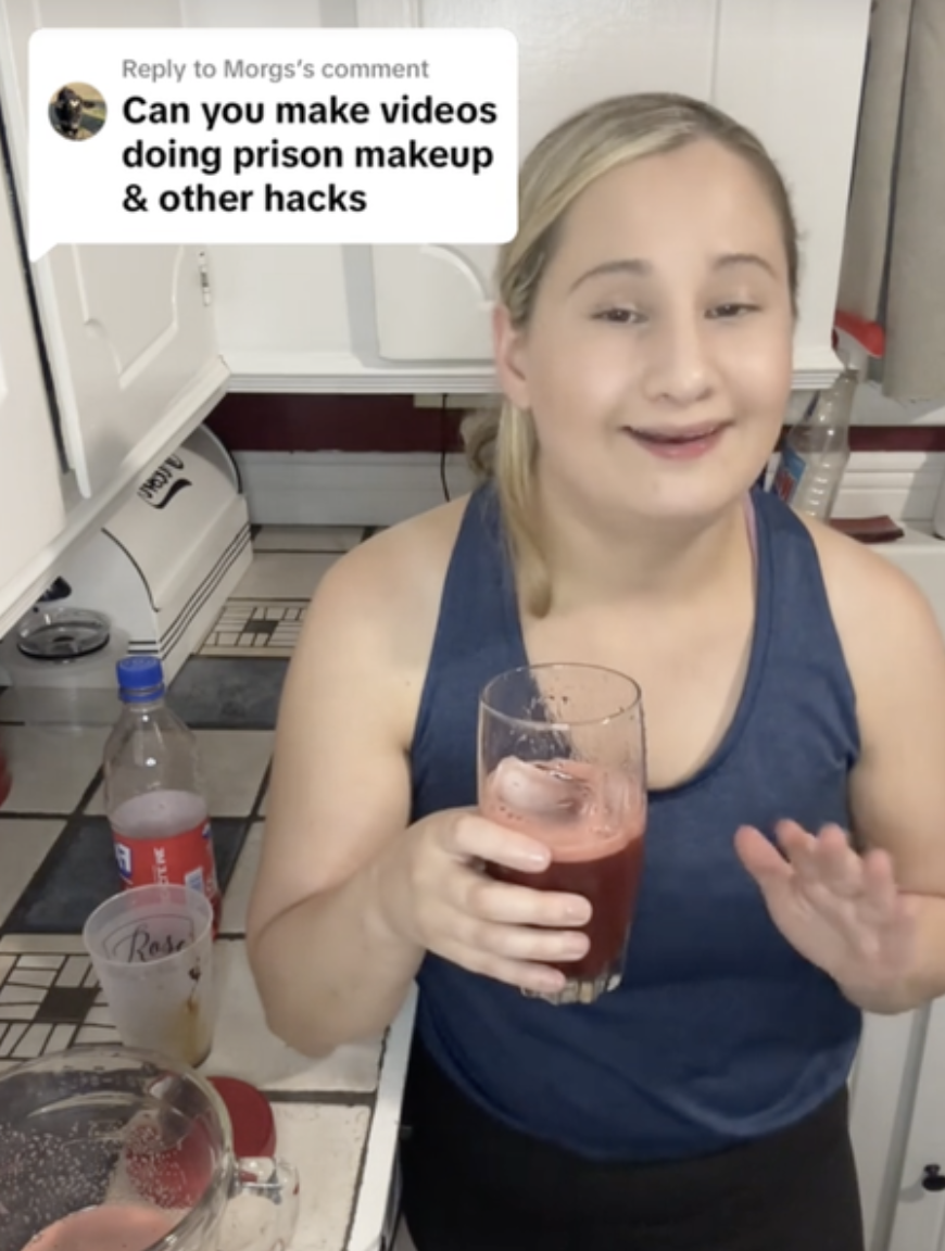 Gypsy is standing in kitchen holding a glass with a pink drink