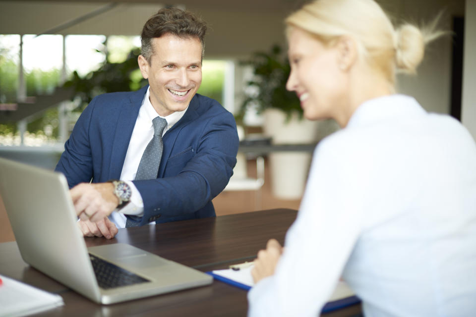 Two smiling business people share information on a laptop screen.