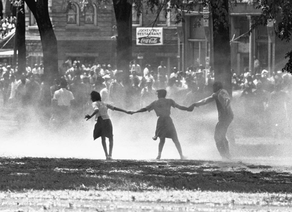 Three demonstrators join hands to build strength against the force of water sprayed by riot police in Birmingham, Alabama, during a protest of segregation practices in May of 1963.