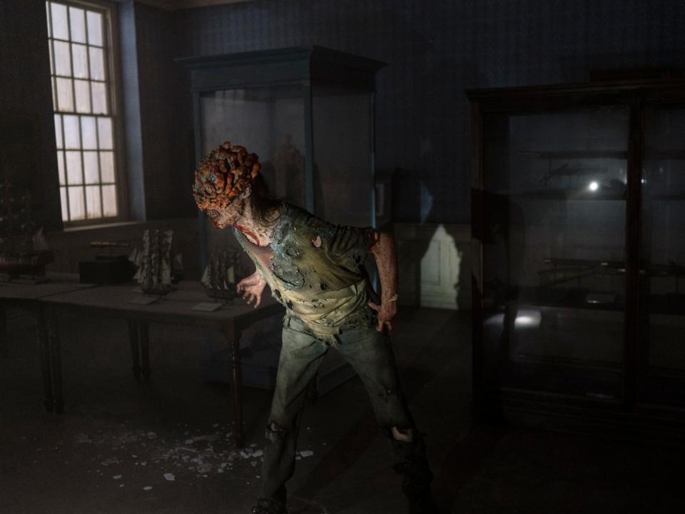 a clicker in the last of us. it's a zombie-like infected being with fungal growth on its head, in a stance as if it's attempting to stalk its prey.