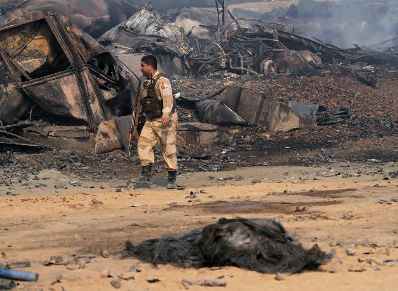 An Afghan security officer walks past burnt tankers in Islam Qala