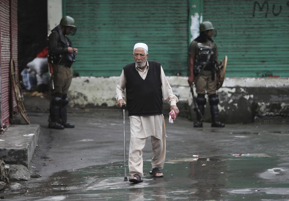 FILE- In this Aug. 10, 2019 file photo, an elderly Kashmiri man crosses a road as Indian paramilitary soldiers stand guard in Srinagar, Indian controlled Kashmir. The region outperforms India on measures such as life expectancy, literacy and poverty, and its economy has been growing steadily this decade, in spite of frequent skirmishes between militants and security forces that have temporarily halted commercial activity. (AP Photo/Mukhtar Khan, File)