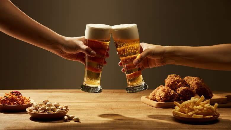 Toasting pints of beer over a table with fries and chicken