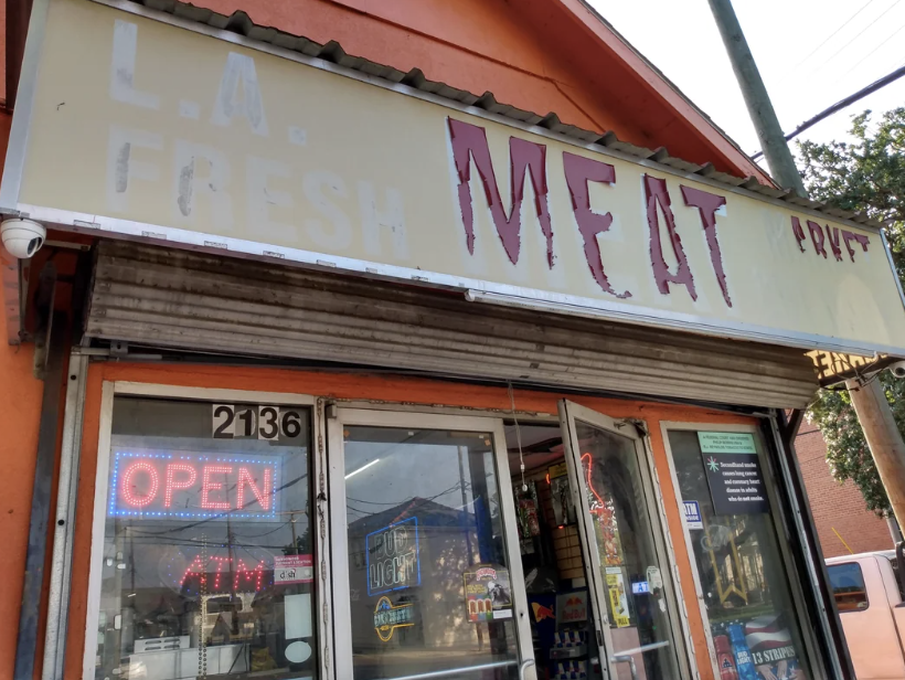 Storefront of "L.A. Fresh Meat" with signs indicating it is open and has an ATM. The store has a large window displaying various posters and products