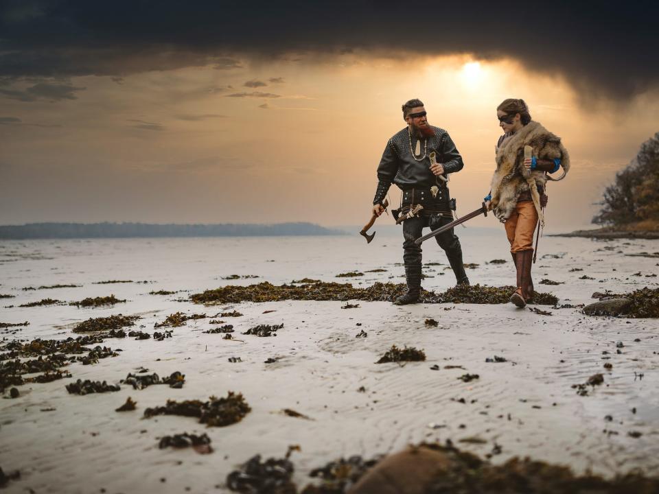 A couple stand on icy terrain in traditional Viking attire.