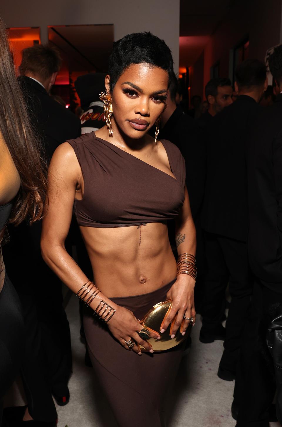 Teyana Taylor in a fitted, sleeveless dress, with gold accessories, at an event