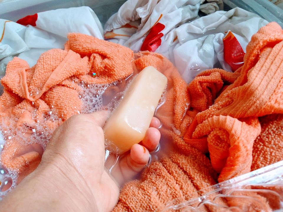 A hand washes orange towels with a bar of soap