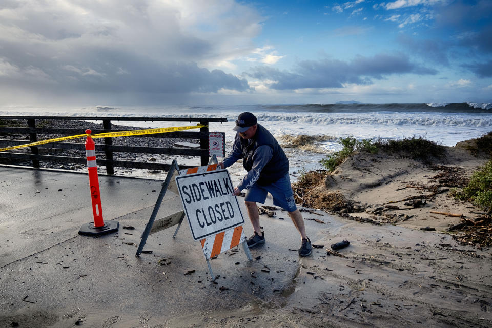 A Ventura city worker places a closed sign at a sea wall where rough surf breaks near the Ventura pier on Saturday, Dec. 30, 2023 in Ventura, Calif. Bulldozers built giant sand berms to protect beachfront homes in Ventura, one of California's coastal cities hit hard this week by extraordinary waves generated by powerful swells from Pacific storms. (AP Photo/Richard Vogel)