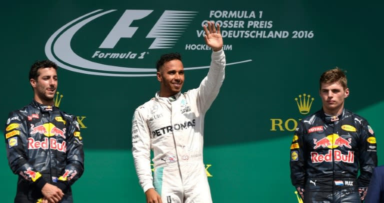 Mercedes driver Lewis Hamilton (C) waves on the podium next to Red Bull Racing's Daniel Ricciardo (L) amd Max Verstappen after winning the German Grand Prix