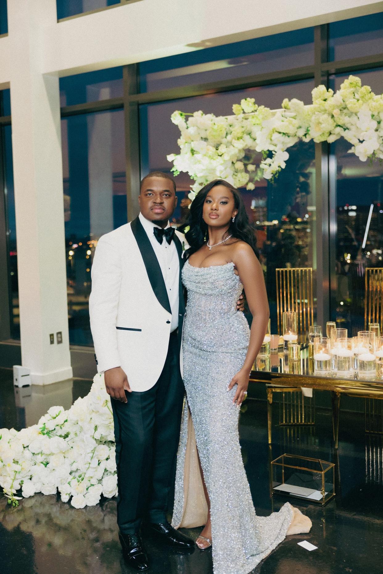 A bride and groom pose in front of a floral archway.