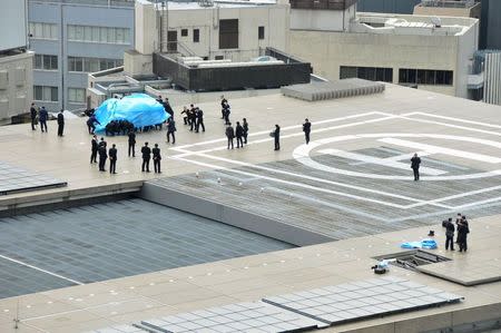 Police and security officers investigate an unidentified drone (L, under blue cover) which was found on the rooftop of Prime Minister Shinzo Abe's official residence in Tokyo, in this photo taken by Kyodo April 22, 2015. Mandatory credit REUTERS/Kyodo