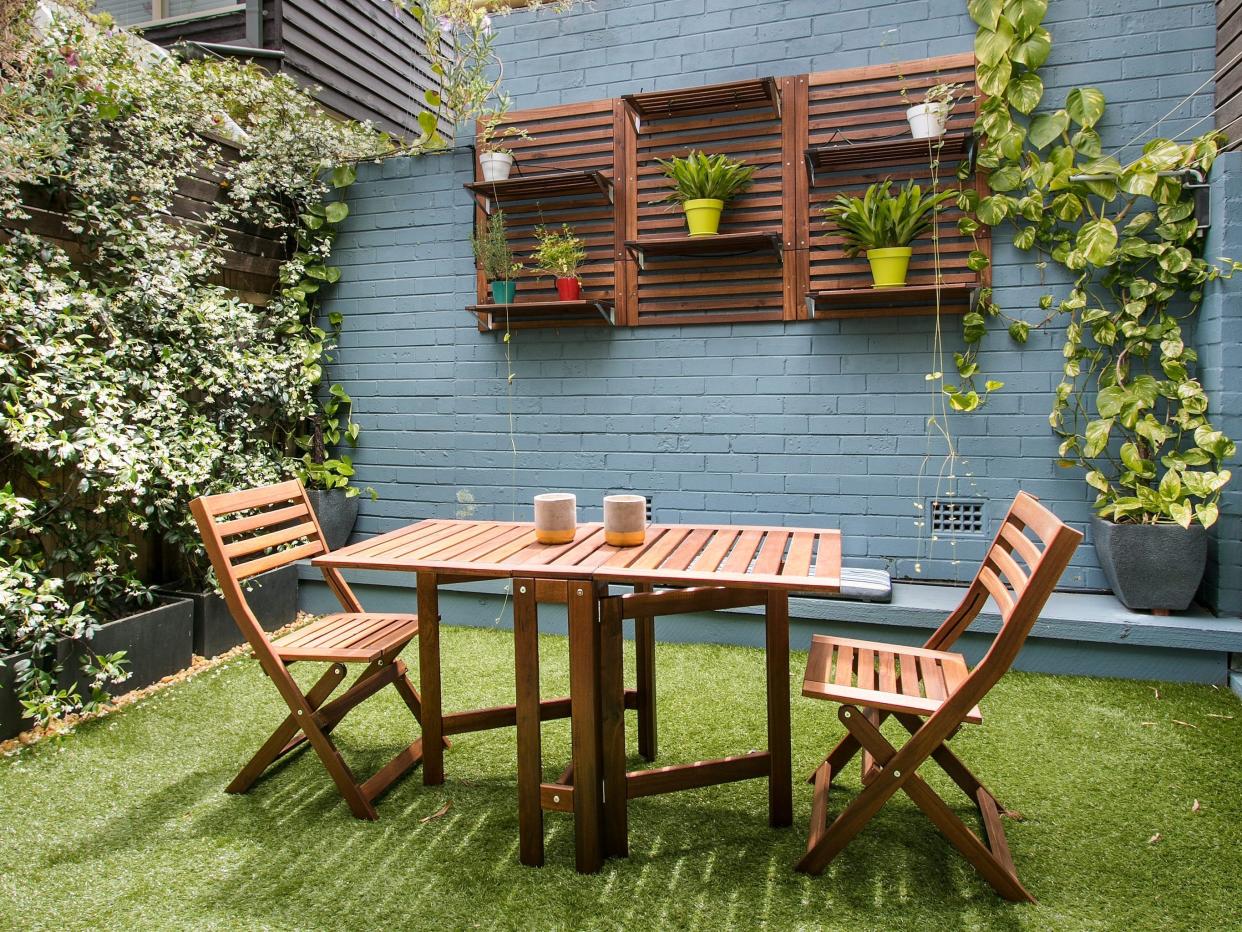 outdoor area with greenery, grass, and a brown table with matching chairs, all surrounded by blue walls