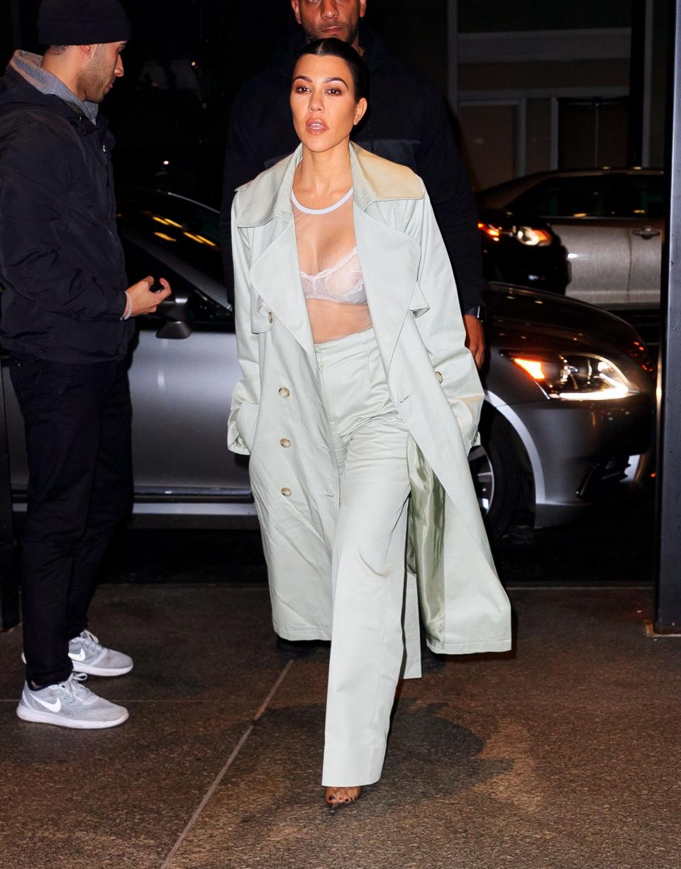 Kourtney in a mint green trench coat, matching high-waisted trousers, and a sheer white mesh bralette.