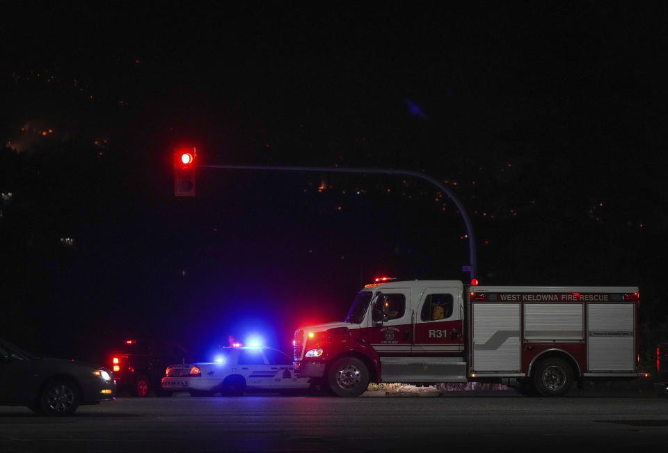 Firefighters wait to pass through an RCMP roadblock as the McDougall Creek wildfire burns on the mountainside above houses in West Kelowna, B.C., on Friday, Aug. 18, 2023. Thousands have fled, driving hundreds of kilometers (miles) to safety or waiting in long lines for emergency flights, as the worst fire season on record in Canada showed no signs of easing. (Darryl Dyck /The Canadian Press via AP)