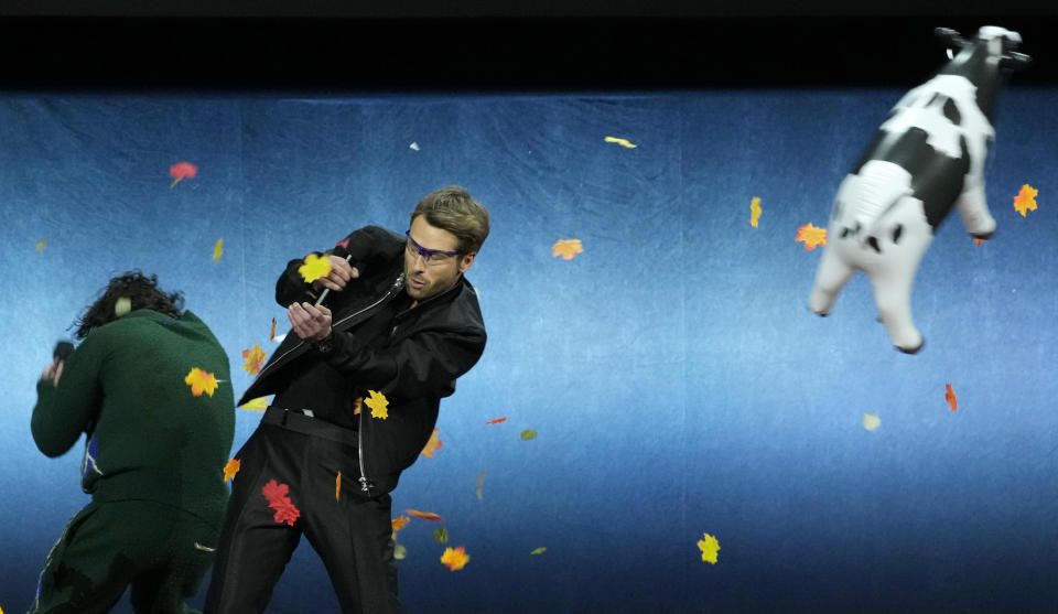 Glen Powell, second from left, and Anthony Ramos, cast members in the upcoming film "Twisters," dodge a fake cow and flying leaves from a wind machine onstage during the Universal Pictures and Focus Features presentation at CinemaCon 2024, Wednesday, April 10, 2024, at Caesars Palace in Las Vegas. (AP Photo/Chris Pizzello)