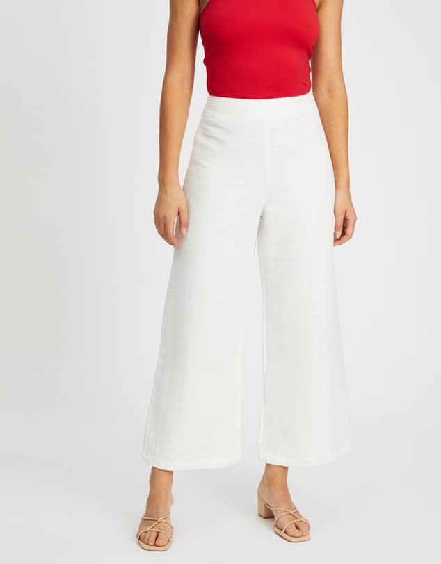 A shoulder-down view of a model wearing a red tank top over white Indra Wide Leg Pants, $55, from Atmos & Here at The Iconic 