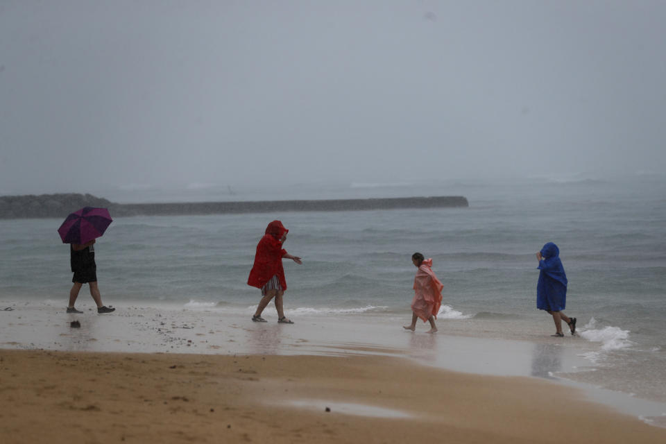 Beach goers play in the rain on Waikiki Beach, Monday, Dec. 6, 2021, in Honolulu. A strong storm packing high winds and extremely heavy rain flooded roads and downed power lines and tree branches across Hawaii, with officials warning Monday of potentially worse conditions ahead. (AP Photo/Marco Garcia)