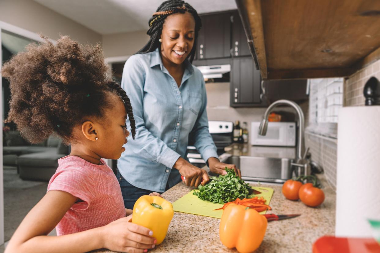 mother and daughter making a salad, cutting vegetables in kitchen