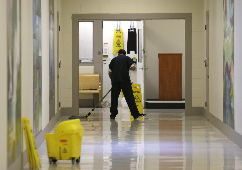 FILE - In this June 21, 2017, file photo, a detainee mops a floor in a hallway of the Northwest Detention Center in Tacoma, Wash., during a media tour of the facility. The Trump administration is opposing Washington state’s effort to make a privately run, for-profit immigration jail pay detainees minimum wage for the work they do. Washington Attorney General Bob Ferguson sued The GEO Group in 2017, saying its Northwest Detention Center in Tacoma must pay the state minimum wage to detainees who perform kitchen, janitorial and other tasks. (AP Photo/Ted S. Warren, File)