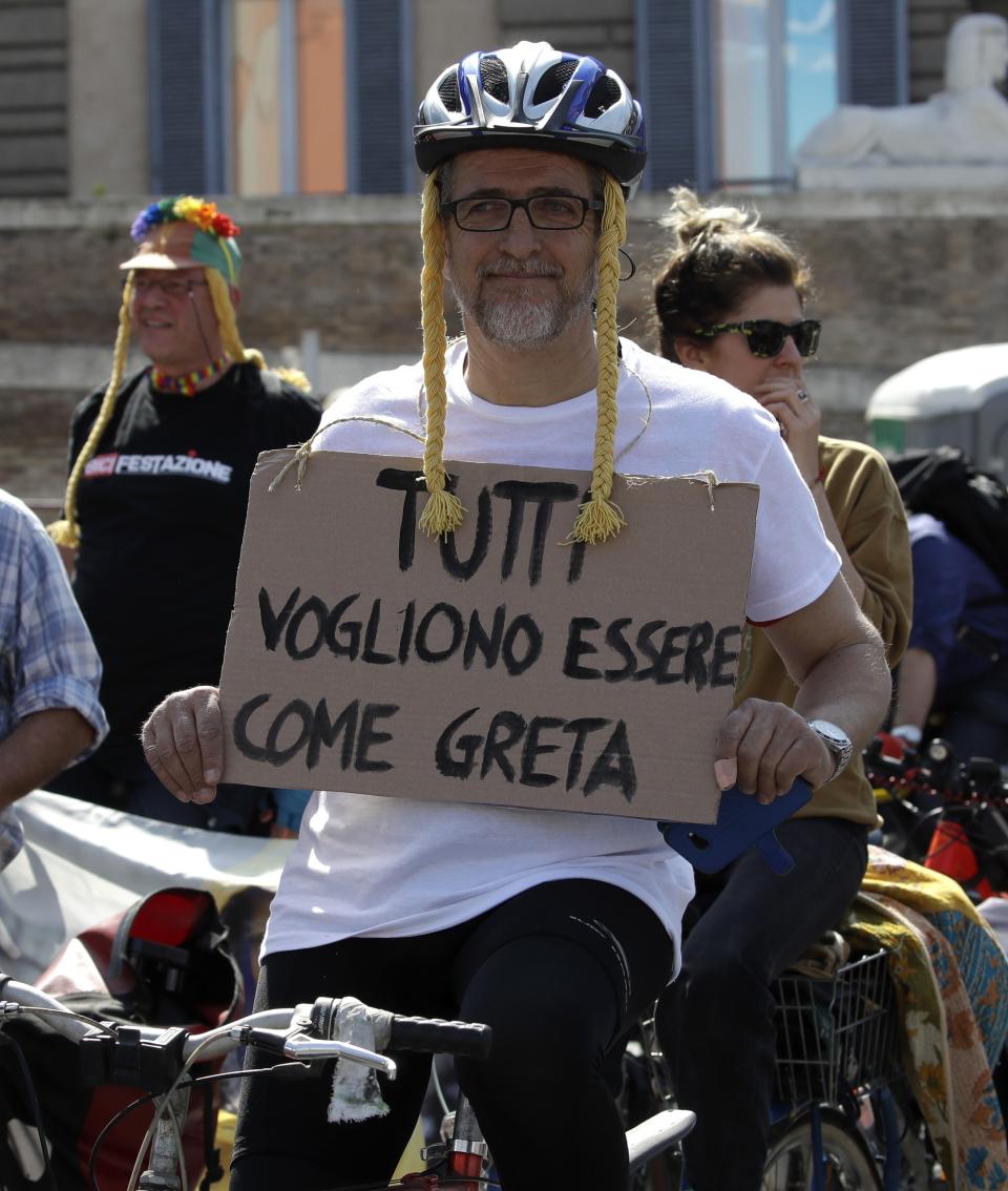 A man wearing a wig with braids holds up a sign with writing reading in Italian "Everyone wants to be like Greta", referring to Swedish teenager and environmental activist Greta Thunberg, during a Fridays for Future demonstration, in Rome, Friday, April 19, 2019. Volunteers pedaled on fixed bicycles to supply energy for the stage during the rally. (AP Photo/Alessandra Tarantino)