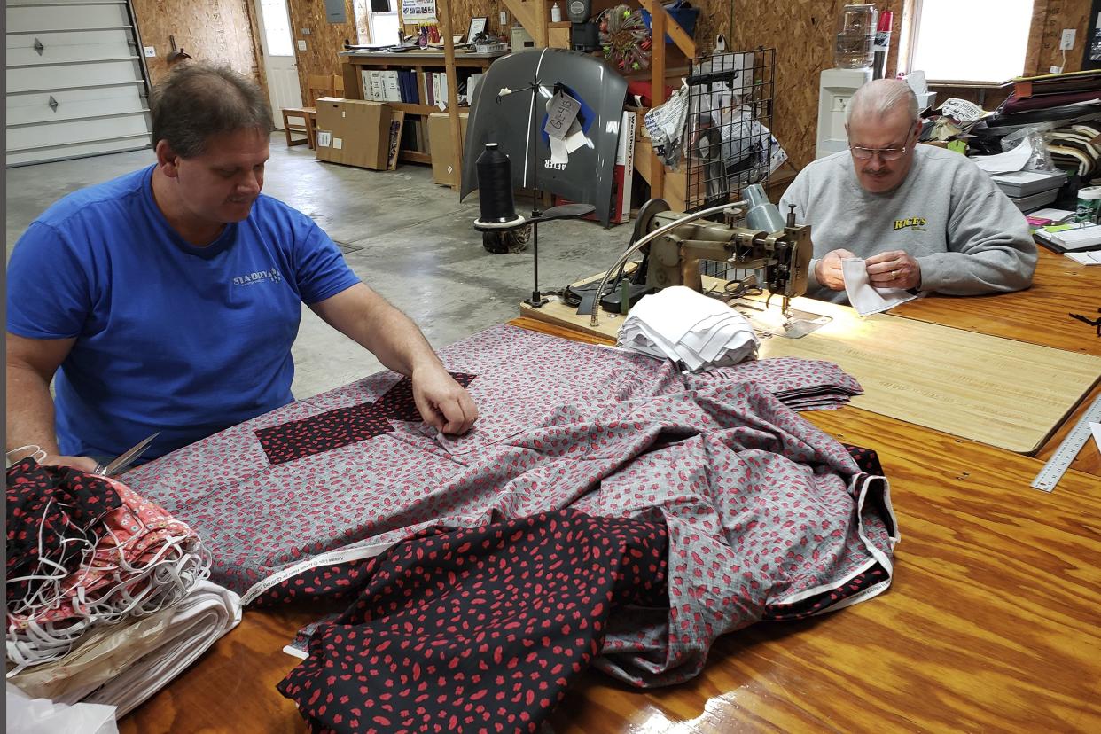 Bill Purdue, left, cuts pieces of fabric while Mike Rice sews them into face masks in Rice's autobody and upholstery shop in Washington, Ind. on Sunday, March 22, 2020. They will deliver the masks this week to Deaconess Health System in Evansville, Indiana, which asked community members to sew cloth masks for health care workers who may face a shortage amid the coronavirus pandemic. They're among legions of everyday Americans making face masks for desperate hospitals, nursing homes and homeless shelters that could run out of personal protective equipment.