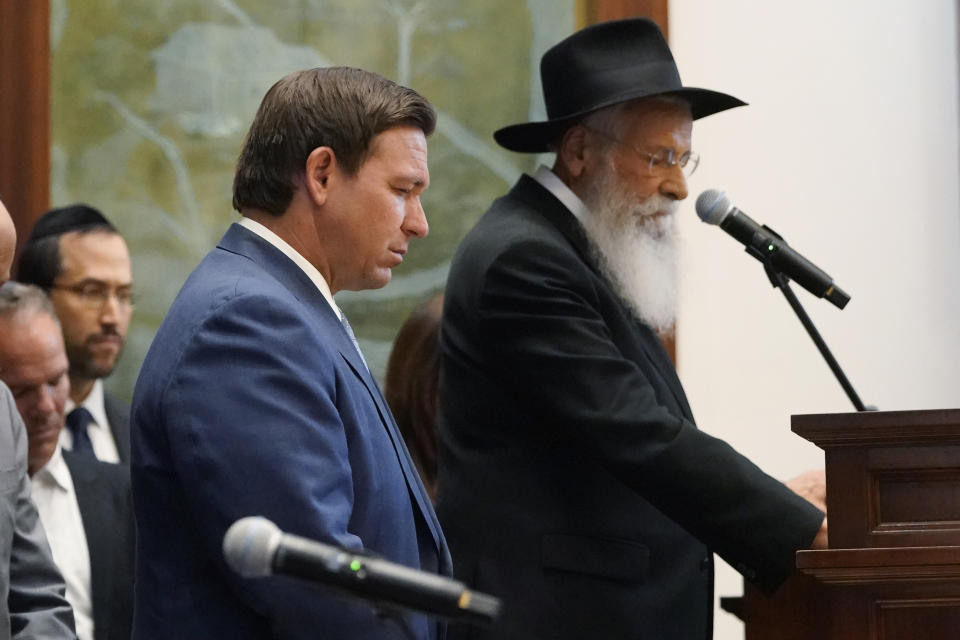 FILE - Rabbi Sholom Lipskar, Florida Gov. Ron DeSantis, left, and others participate in a moment of silence, Monday, June 14, 2021, at the Shul of Bal Harbour, a Jewish community center in Surfside, Fla. Lipskar says he tells congregation members that COVID-19 vaccination should be a matter of free choice. “But I always recommend that they get a medical opinion from a competent professional,” he added. “In a serious matter, they should get two concurring medical opinions.” (AP Photo/Wilfredo Lee, File)