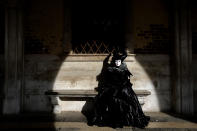 FILE - In this Feb. 16, 2020 file photo, a woman wearing a carnival costume sits on a bench of the Palazzo Ducale during carnival celebrations in Venice, Italy, Sunday, Feb. 16, 2020. Still reeling from the effects of major flooding just a few months ago, Venice faces a new emergency: the threat of a new virus outbreak across Italy that is scaring international visitors world-wide and hitting the economy hard. (AP Photo/ Luca Bruno)