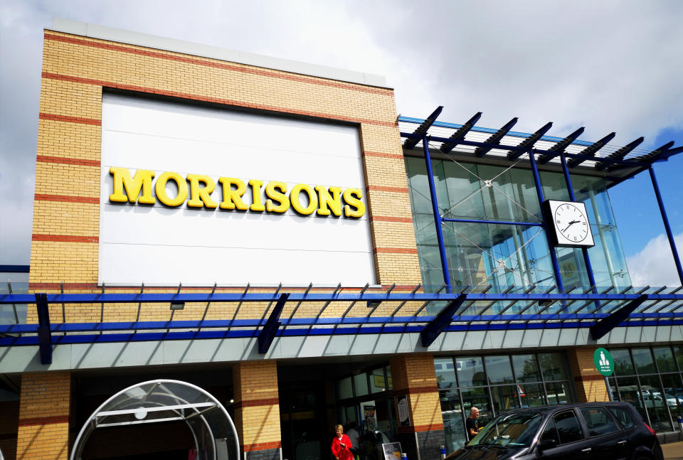 Swansea, UK: August 06, 2019: Main entrance to a Morrisons superstore. Morrisons is the fourth largest chain of supermarkets in the United Kingdom. A customer walks out of the shop.