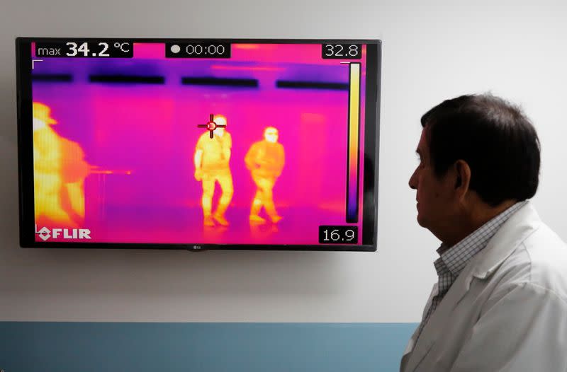 A doctor looks to a monitor showing thermal scanners that detect temperatures of passengers at the security check inside the airport in Guatemala City