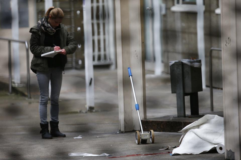 Police officer examines crime scene next to covered body at entrance to courthouse in Frankfurt