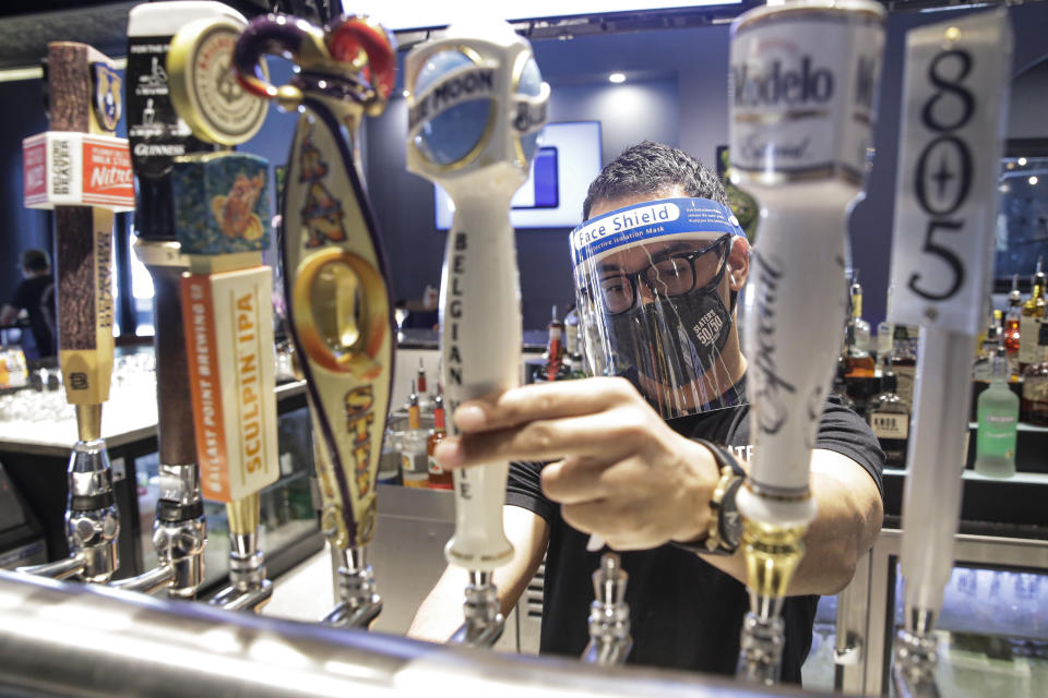 A bartender pours a beer while wearing a mask and face shield amid the coronavirus pandemic at Slater's 50/50 Wednesday, July 1, 2020, in Santa Clarita, Calif. California Gov. Gavin Newsom has ordered a three-week closure of bars, indoor dining and indoor operations of several other types of businesses in various counties, including Los Angeles, as the state deals with increasing coronavirus cases and hospitalizations. (AP Photo/Marcio Jose Sanchez)