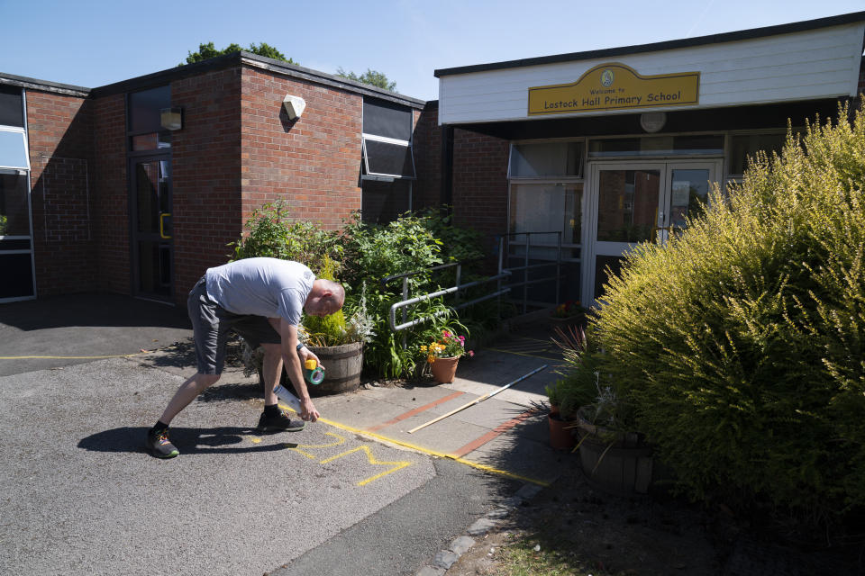 David Waugh, head teacher at Poynton High School and Education Trust Leader sprays safe distance markers on the ground as measures are taken to prevent the transmission of coronavirus before the possible reopening of Lostock Hall Primary school in Poynton near Manchester, England, Wednesday May 20, 2020. (AP Photo/Jon Super)