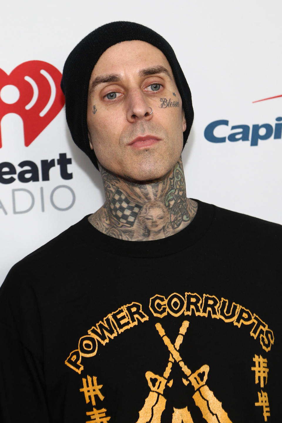 Travis on a red carpet in a beanie and a Power Corrupts shirt