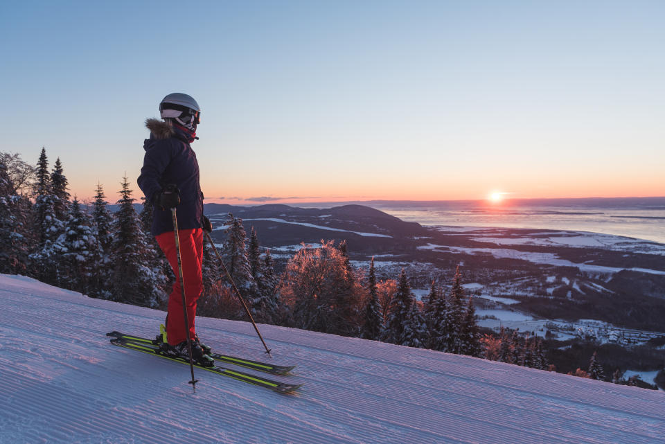 Skier takes in the view from a Québec ski resort summit at sunset, in Mont-Sainte-Anne, Québec