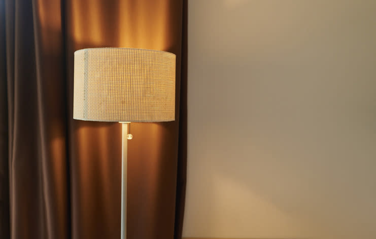 A lit floor lamp stands beside a brown curtain, casting a warm glow