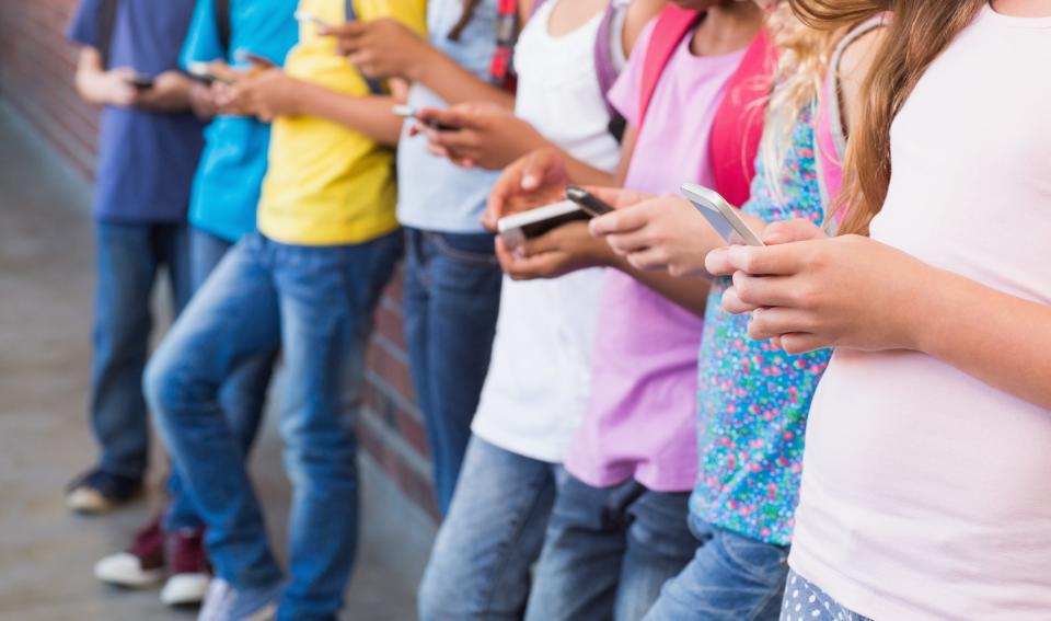 A group of kids leaning against a wall, all looking down at their smartphones, engrossed in their screens